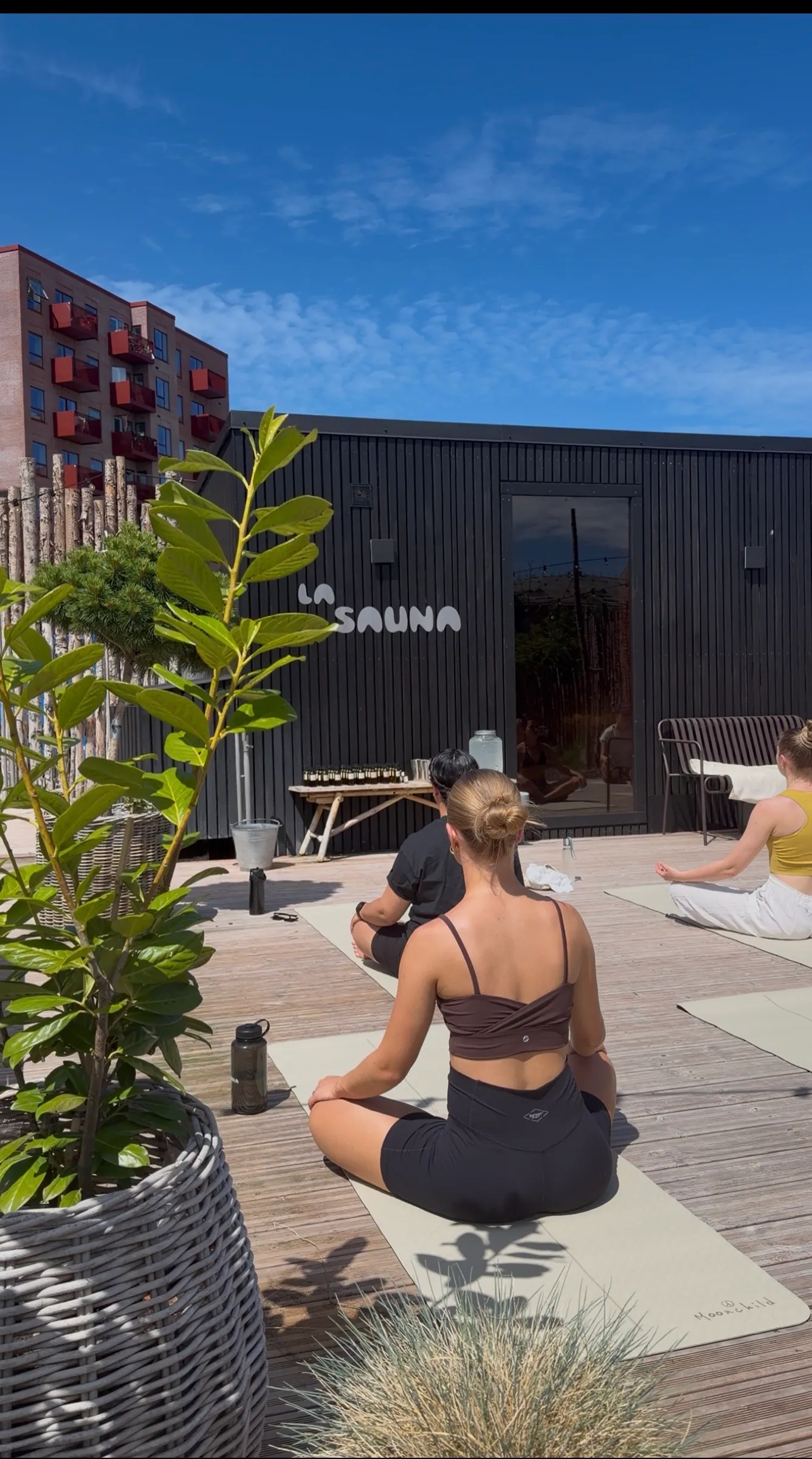 Yoga på terrassen foran den sorte saunakabine med La Sauna-skiltet