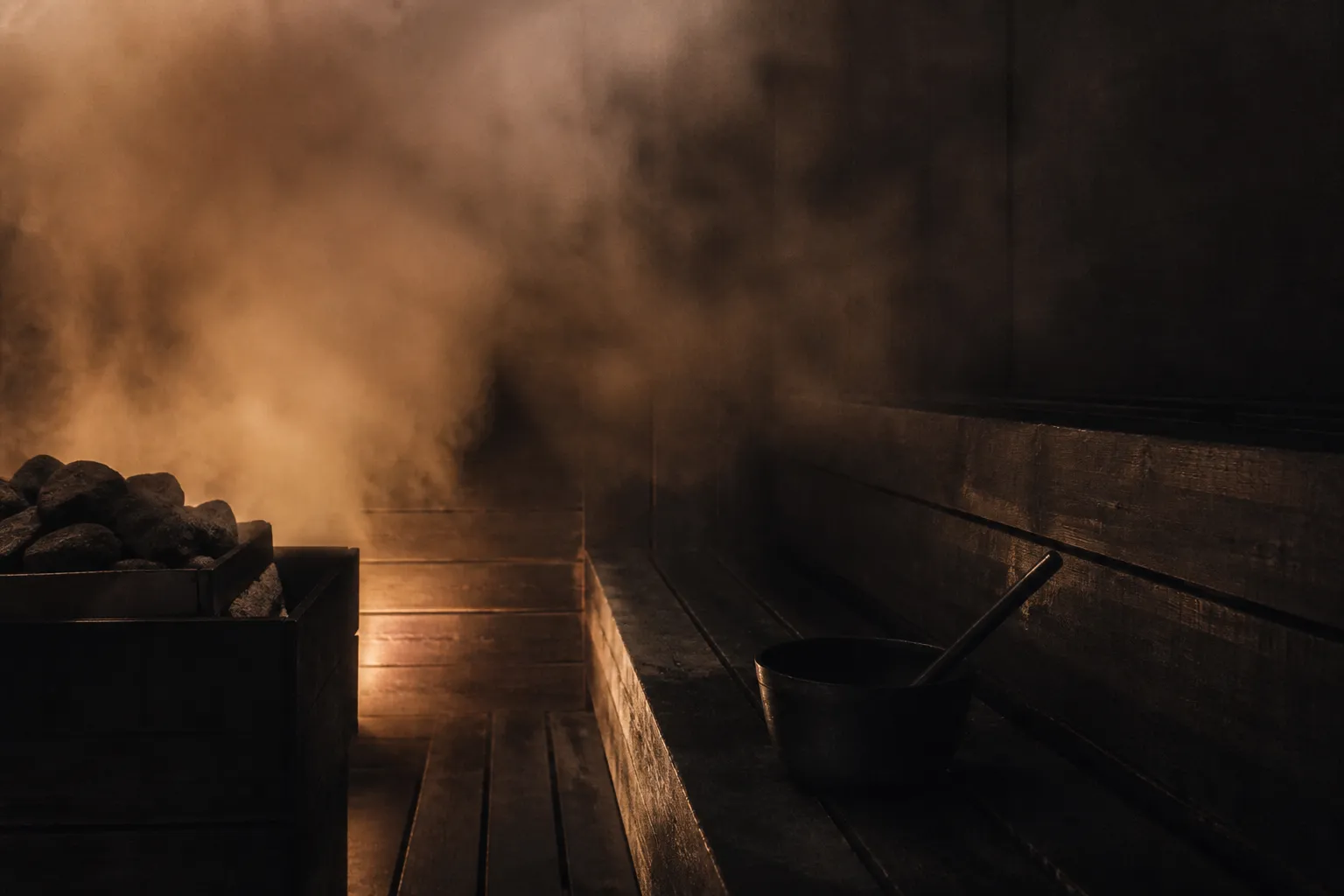 Mørk sauna med damp der stiger op fra de varme sten, og en øse på bænken