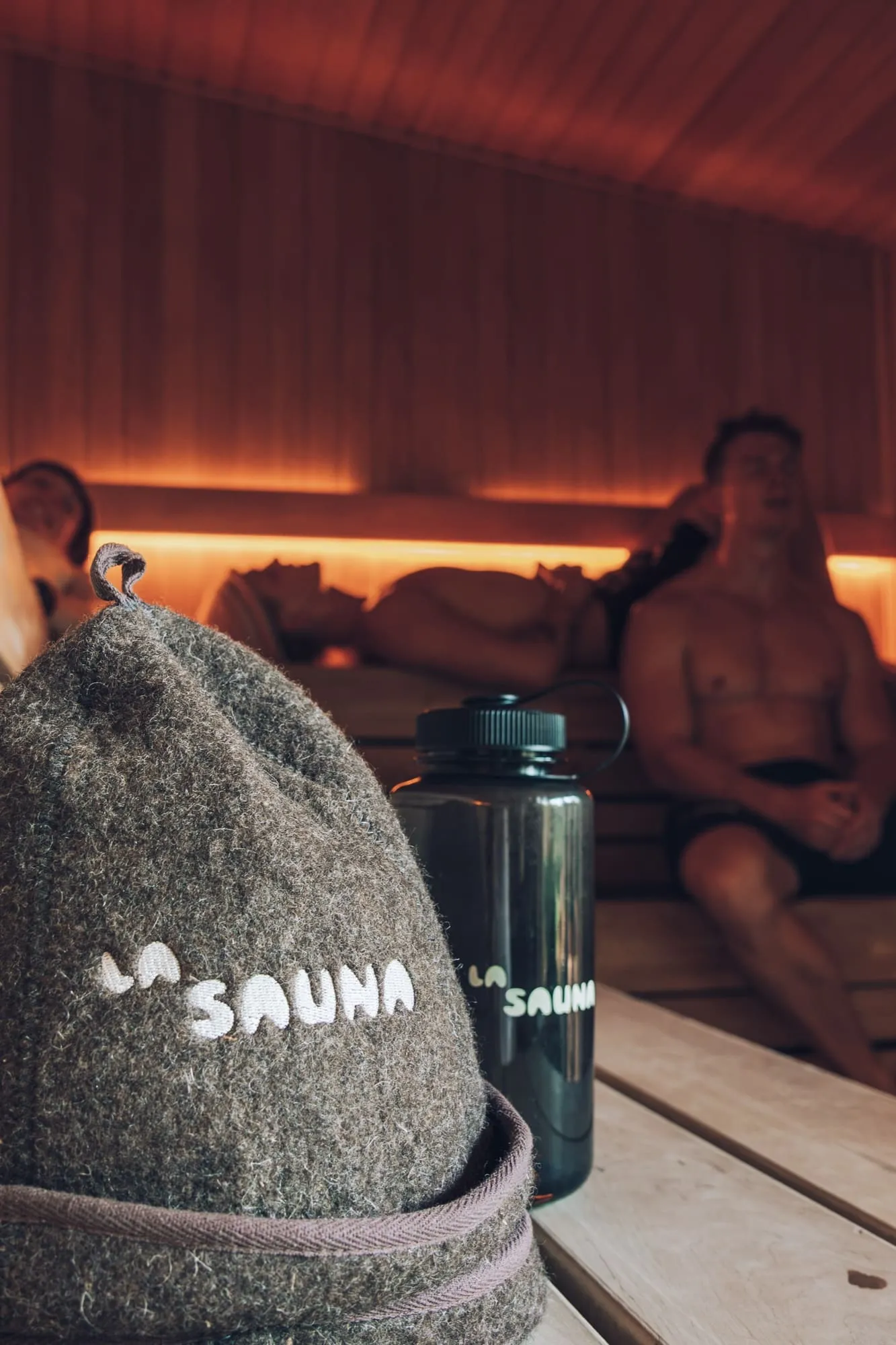 La Sauna-uldhat og drikkedunk på bænken, mens gæster hviler i baggrunden